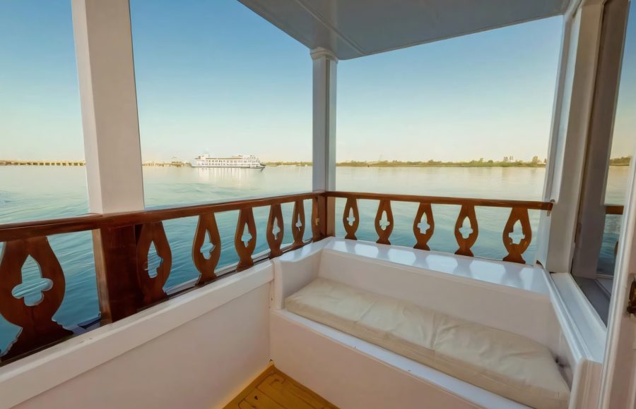 Small white balcony on a boat with a wooden railing and a cushioned bench.