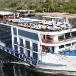 A large white Nile cruise ship on the water near a lush green bank.