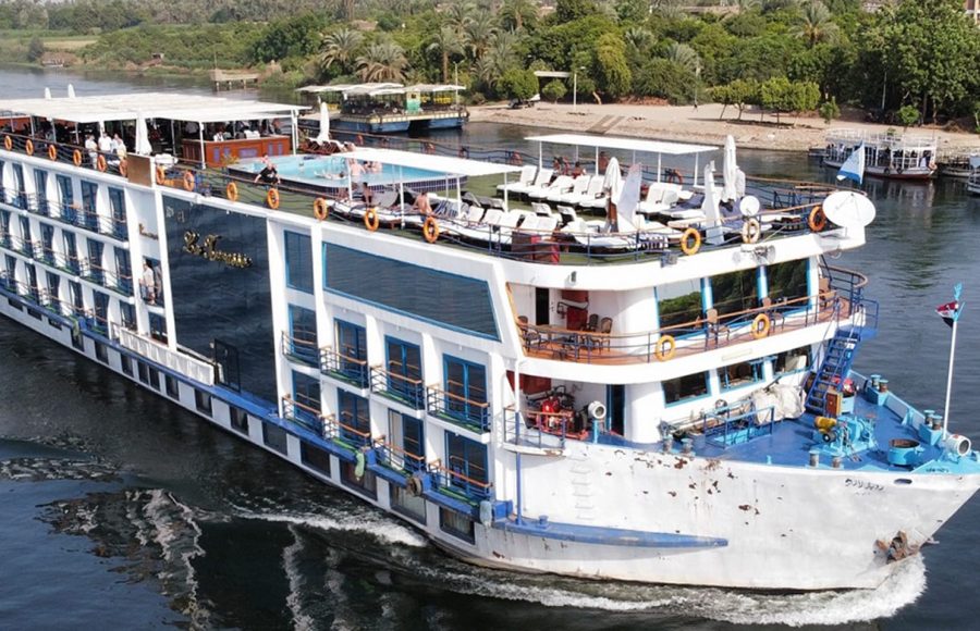 A large white Nile cruise ship on the water near a lush green bank.