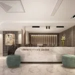 Modern cruise ship reception desk made of white marble, labeled "Liberty Story Cruise," flanked by two round turquoise ottomans.