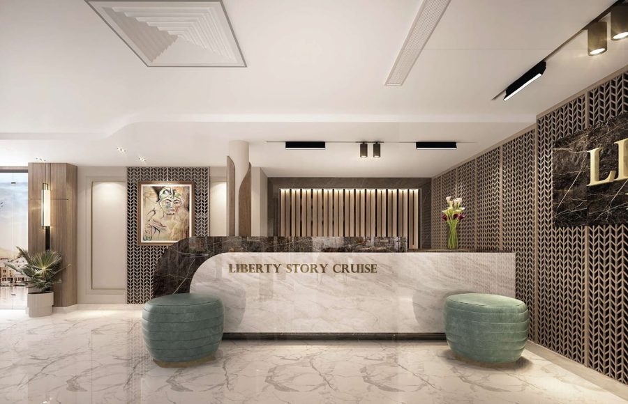 Modern cruise ship reception desk made of white marble, labeled "Liberty Story Cruise," flanked by two round turquoise ottomans.
