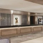 Long, wood-paneled cruise ship reception counter with a black top, framed by patterned screens and Egyptian-themed artwork.