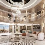Wide view of a luxurious, circular, two-story cruise ship atrium with curved sofas, a grand chandelier, and light wood and gold accents.