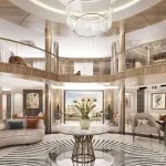 Luxurious, circular two-story cruise ship atrium/reception lobby with modern furniture, wood and brass accents, and a large chandelier.