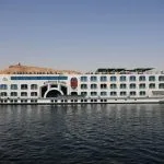 Long shot of the MS Royal Ruby Nile cruise ship with a desert hill in the background.