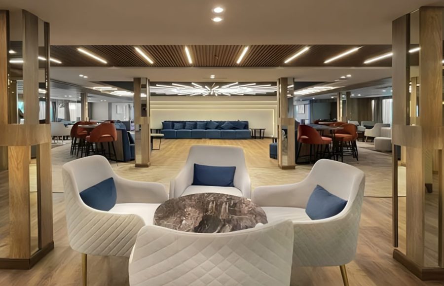Luxurious lounge on MS Royal Signature cruise ship with white armchairs, blue seating, and modern lighting.