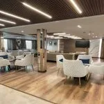 Spacious, modern lounge on MS Royal Signature cruise ship with white armchairs, wood floor, and strip lighting.