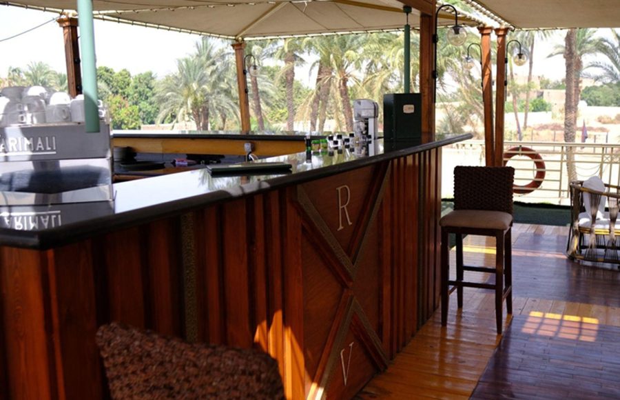 An outdoor wooden bar on the sundeck of the Royal Viking Nile Cruise with a view of palm trees in the background.