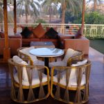 The outdoor sundeck lounge on the Royal Viking Nile Cruise featuring wicker chairs, a large sofa, and a view of palm trees.