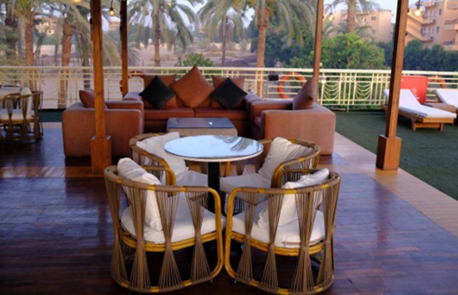 The outdoor sundeck lounge on the Royal Viking Nile Cruise featuring wicker chairs, a large sofa, and a view of palm trees.