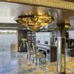 An opulent lounge area with intricate decor and large windows offering views from the Sphinx Nile Cruise
