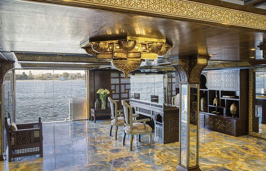 An opulent lounge area with intricate decor and large windows offering views from the Sphinx Nile Cruise