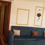 A blue sofa with decorative pillows in a cruise ship cabin, next to a hallway with a red carpet.