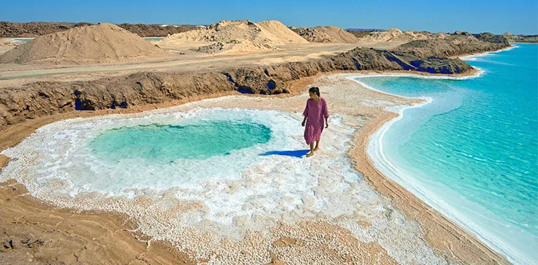A Woman Standing On The White Salt Crust Next To A Bright Turquoise Salt Lake At Siwa Oasis, Egypt.