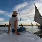A woman in a sun hat enjoys a peaceful Nile cruise with a belly dancer and live entertainment in the distance
