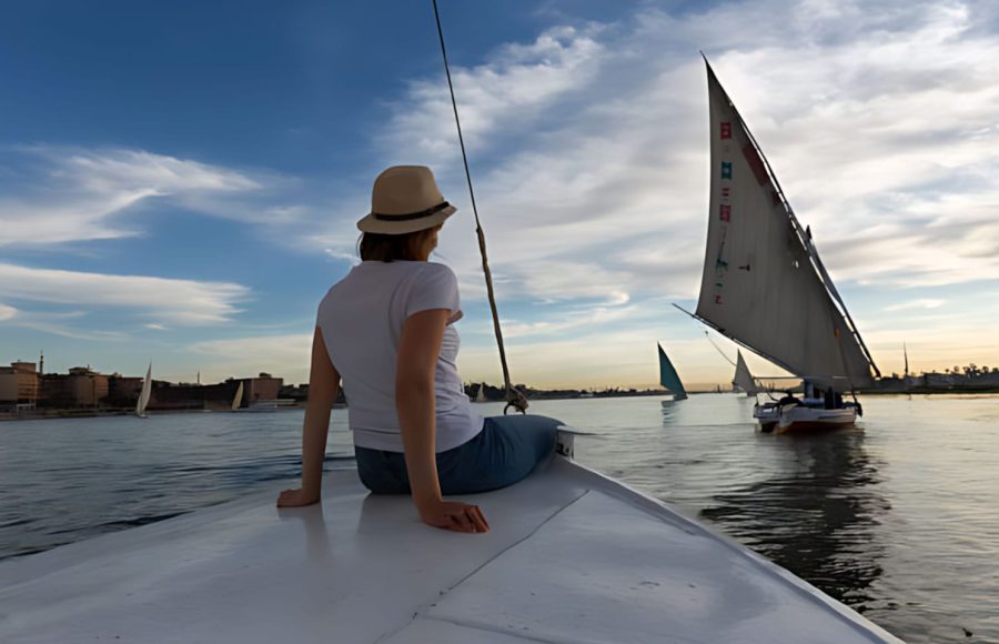 A woman in a sun hat enjoys a peaceful Nile cruise with a belly dancer and live entertainment in the distance