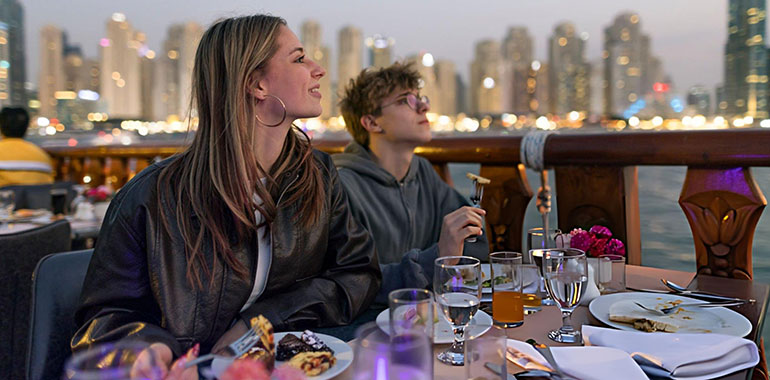 Teenage tourists enjoying Emirati desserts on dhow cruise at Dubai Marina on twilight