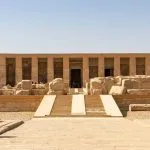 The grand, multi-columned facade and stepped entrance of the Temple of Seti I Abydos in Upper Egypt, a large ancient stone structure in the desert.