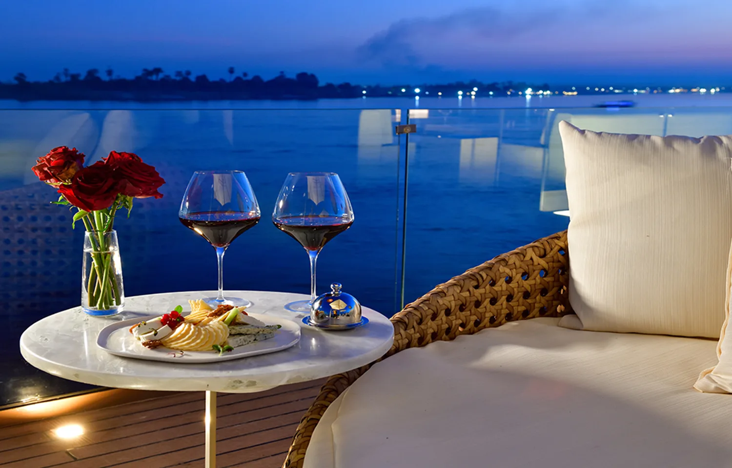 Two glasses of red wine and a cheese platter on a marble side table at twilight.