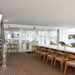 An open-air lounge on a boat deck with a long marble table, wooden chairs, and a staircase.