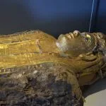 A close-up view of a gold-gilded, painted sarcophagus head and torso displayed in The Mummy Hall at the museum of the golden Mummies in Bahariya Oasis.