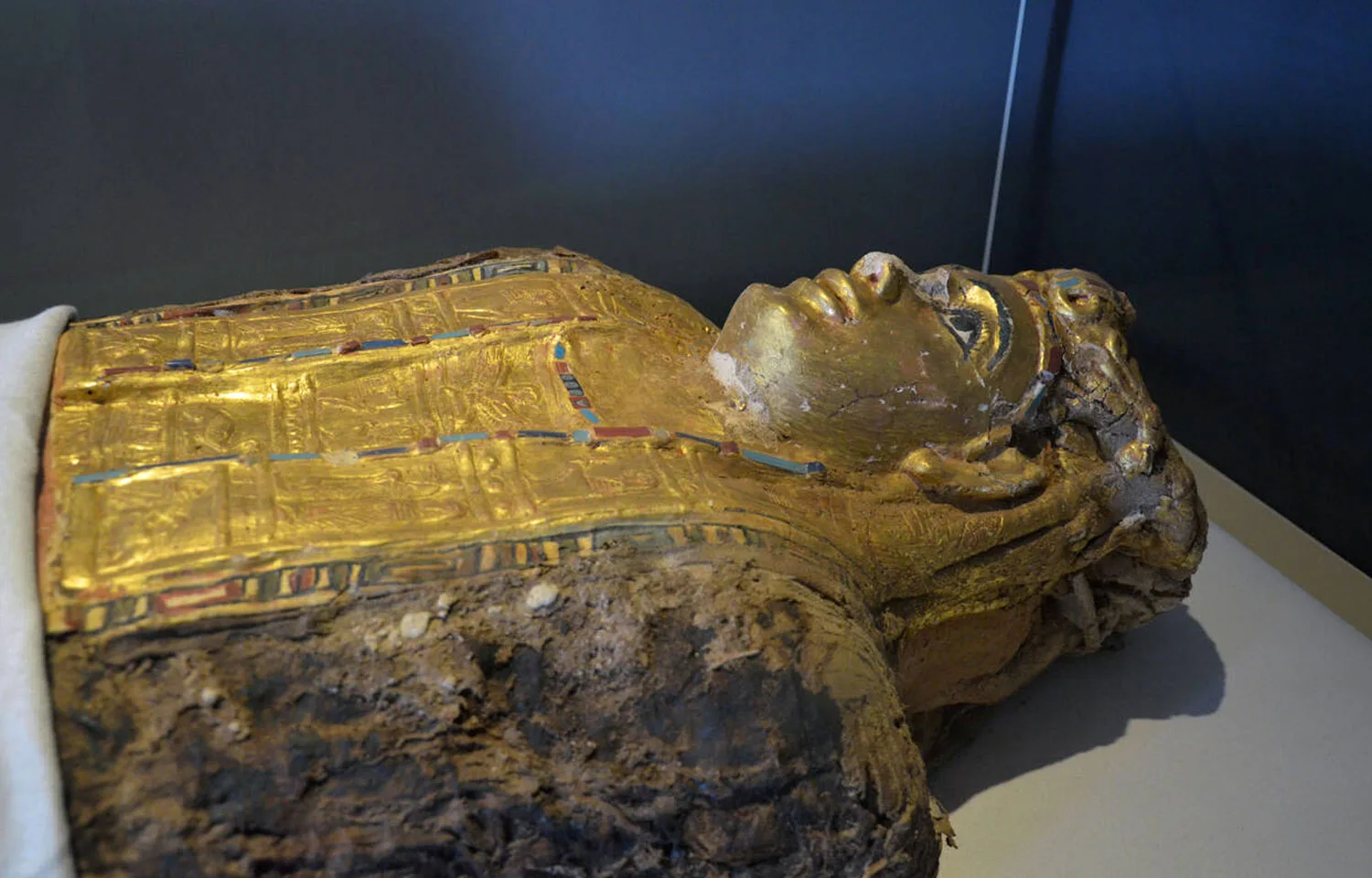A close-up view of a gold-gilded, painted sarcophagus head and torso displayed in The Mummy Hall at the museum of the golden Mummies in Bahariya Oasis.
