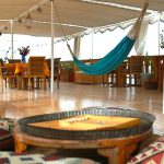 An open-air lounge deck with a turquoise hammock, patterned floor cushions, and a backgammon set.