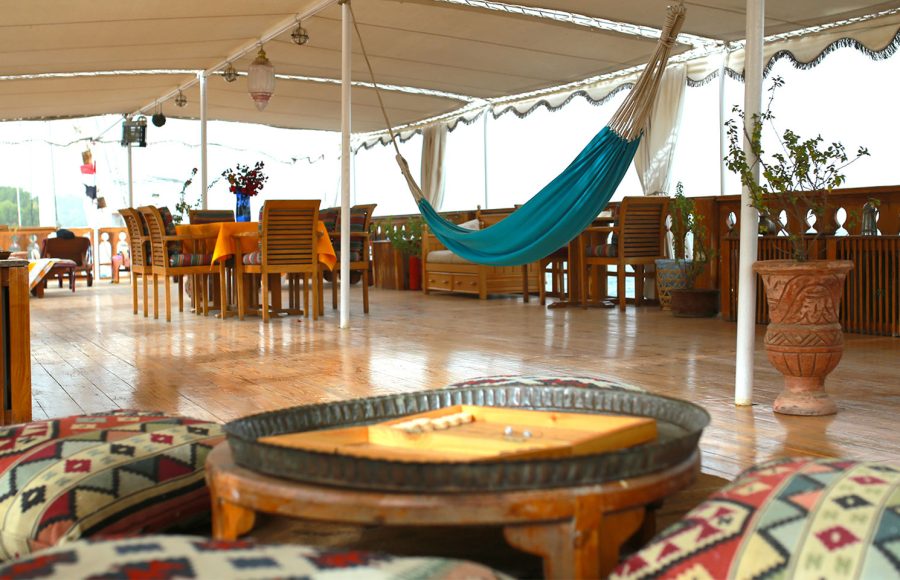 An open-air lounge deck with a turquoise hammock, patterned floor cushions, and a backgammon set.