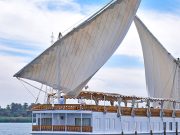 A traditional white Dahabiya sailing boat with two large sails on the Nile River.