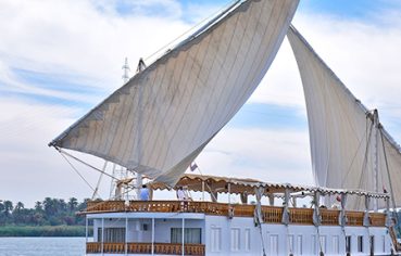 A traditional white Dahabiya sailing boat with two large sails on the Nile River.