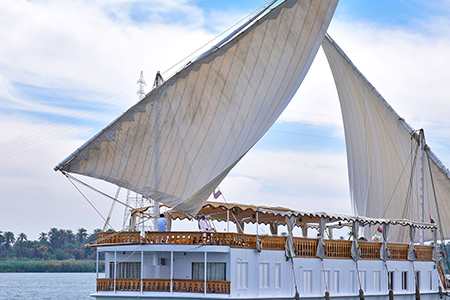 A traditional white Dahabiya sailing boat with two large sails on the Nile River.