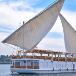 A traditional white Dahabiya sailing boat with two large sails on the Nile River.