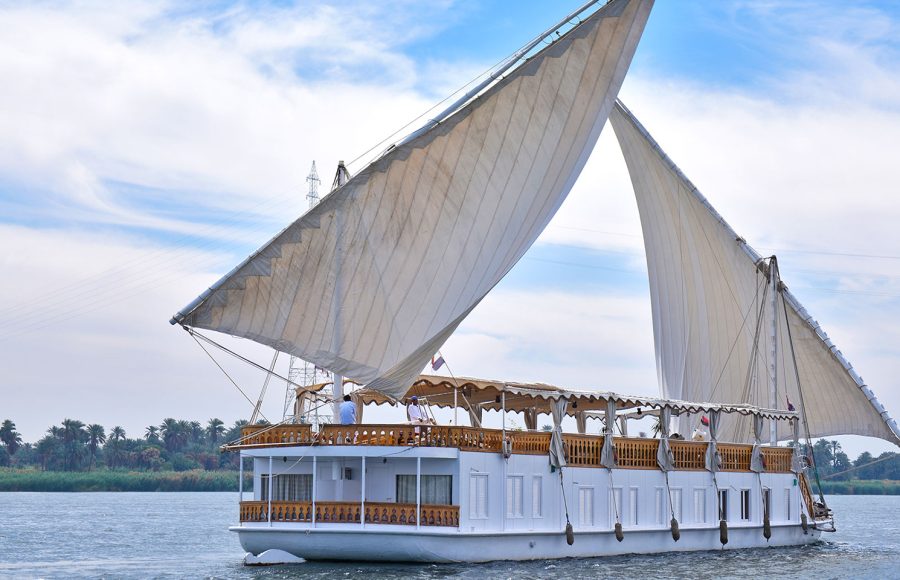 A traditional white Dahabiya sailing boat with two large sails on the Nile River.