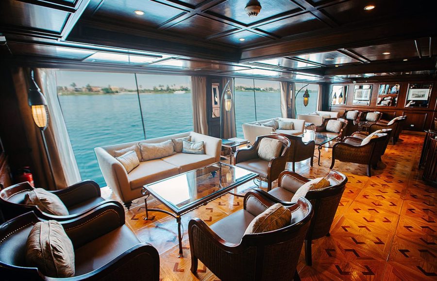 Interior of a luxurious dark wood lounge with panoramic windows on a Nile cruise ship.
