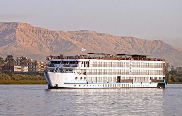 A white Nile cruise ship sailing with hot air balloons and desert mountains in the background.