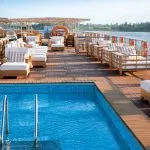 Sunny sun deck of a Nile cruise ship with a pool and wooden lounge chairs.
