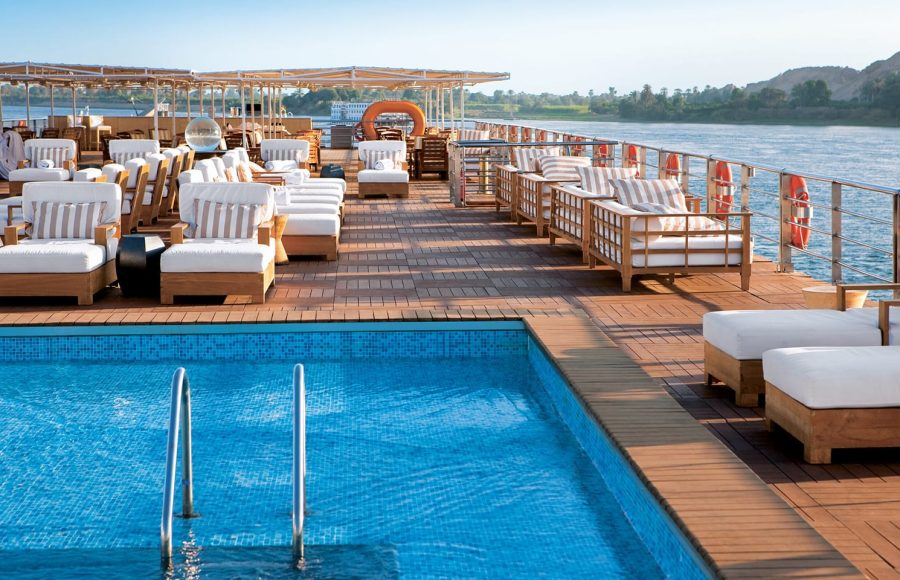 Sunny sun deck of a Nile cruise ship with a pool and wooden lounge chairs.