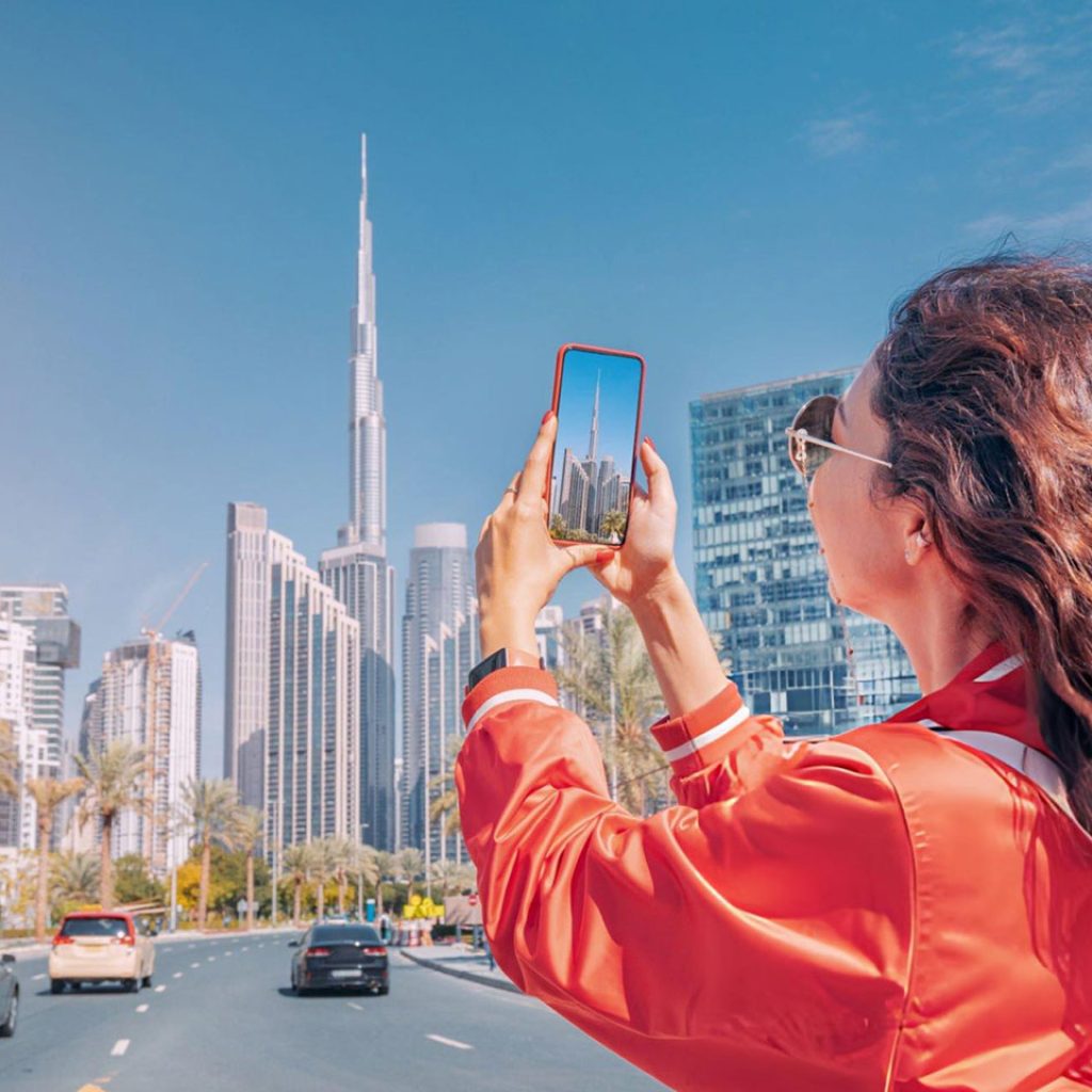 Tourist happy girl taking photos for her travel blog in Dubai downtown district against background of the Burj Khalifa highest skyscraper