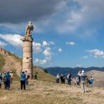 Tourists-admire-a-stone-eagle-statue-sitting-atop-the-southern-column-at-the-ancient-site-of-Karakus-Tumulus-at-Cukurtas-in-Turkiye