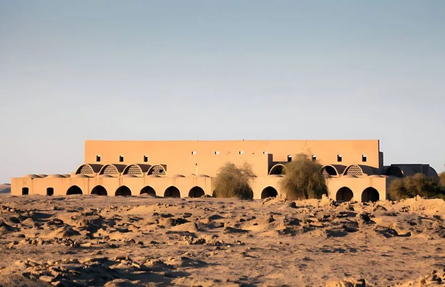 The distinctive, arched mud-brick architecture of the View Of Market Hassan Fathy Designed Village Kharga Oasis Egypt, showing the long, low market building against the clear desert sky.