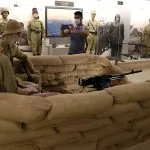 Man takes a picture of a World War II diorama featuring soldiers and a machine gun behind sandbags during a WWII battlefields tour
