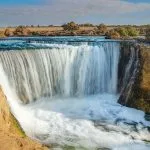 Cascading waterfall in a sunny desert landscape, a key attraction on a Wadi El Rayan tour