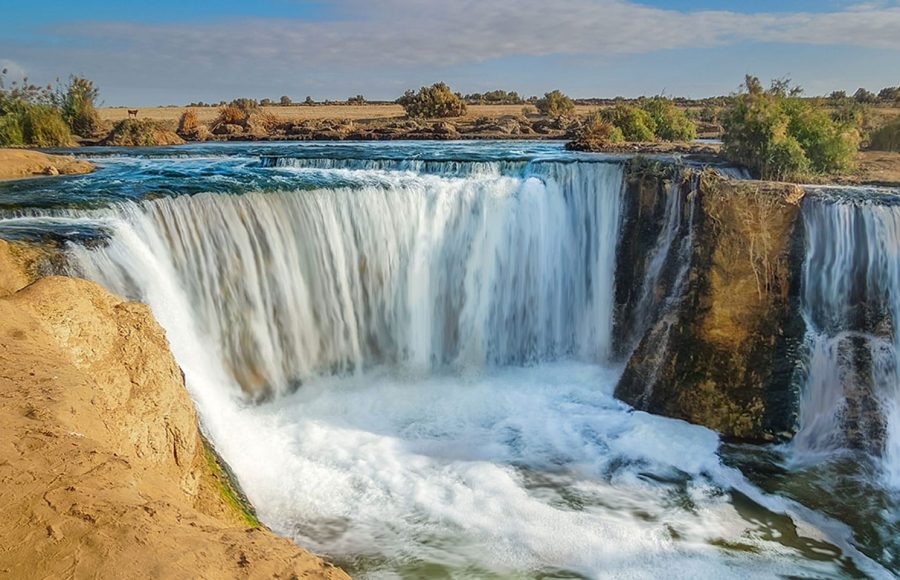 Cascading waterfall in a sunny desert landscape, a key attraction on a Wadi El Rayan tour