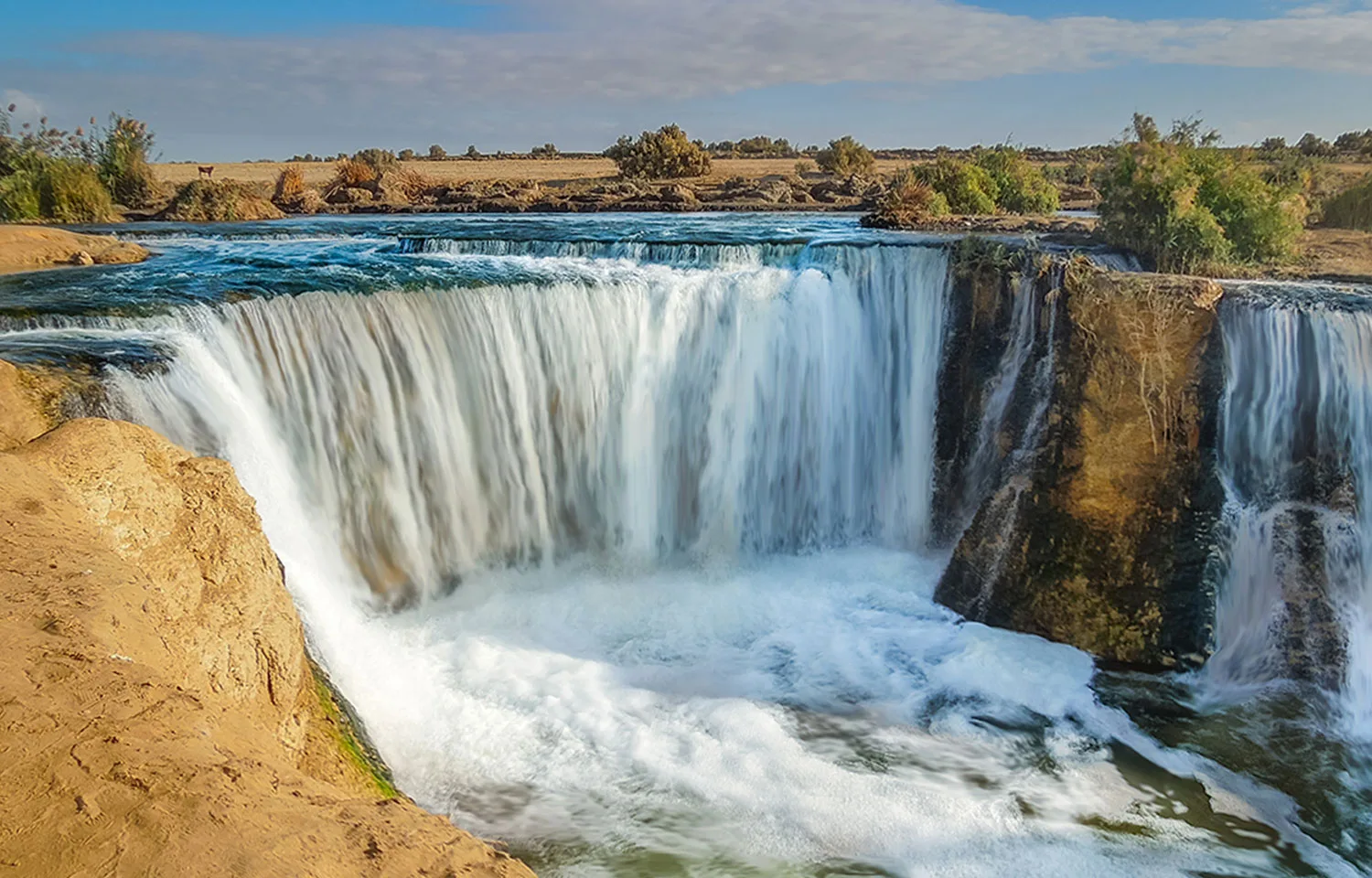 Cascading waterfall in a sunny desert landscape, a key attraction on a Wadi El Rayan tour