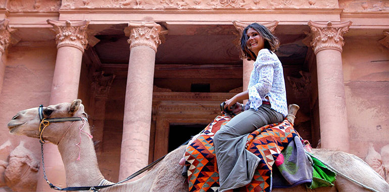 Western Looking Woman Riding A Bedouin Camel And Smiling In Front Of The Treasury In Petra Jordan