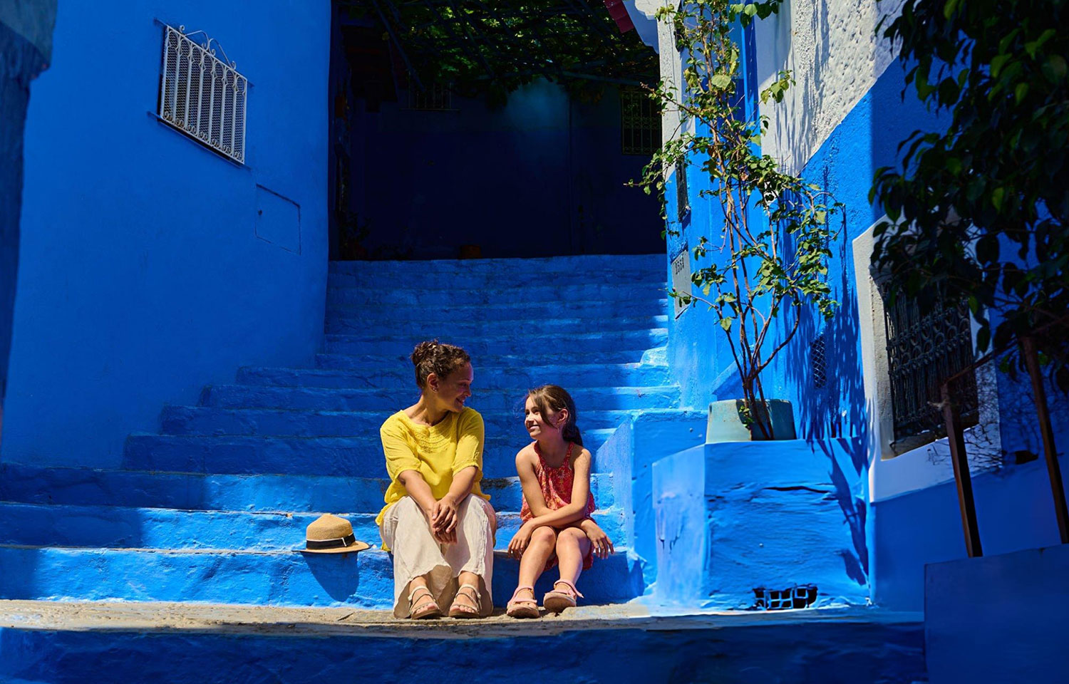 Woman and girl sitting on blue stairs in Chouchaen enjoying travel and warm conversation