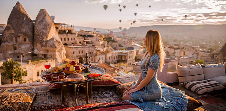 Woman relaxing and drinking turkish tea in Goreme National Park in Cappadocia with hot air ballons in the back ground