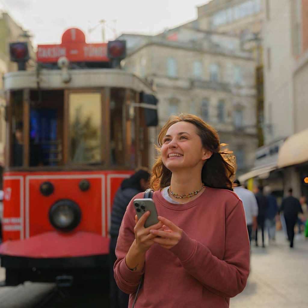 Woman using smartphone walking near the tram in Istanbul enjoing her planning trip to turkey