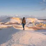 Woman walking across a snow-white landscape in the White Desert, perfect for an Egypt Desert Adventure.