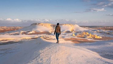 Woman walking across a snow-white landscape in the White Desert, perfect for an Egypt Desert Adventure.